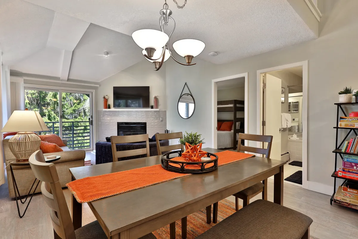 A cozy interior living space with a dining table, a crackling fireplace, a window with scenic views, a decorative mirror, and a well-stocked bookshelf. The mood is intimate and welcoming, ideal for romantic evenings.