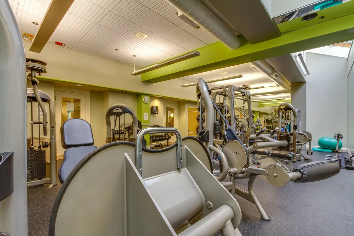 This image showcases a bright, airy fitness center with large windows, modern exercise machines, and free weights. The abundance of natural light and views through the windows hint at the surrounding landscape and the active lifestyle available year-round.