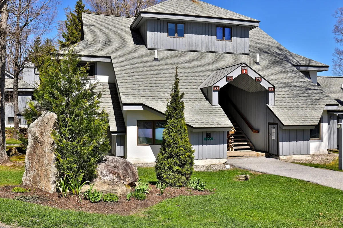 An inviting outdoor view of the building’s architectural details, surrounded by lush greenery and a rock feature in the garden. The scene suggests relaxation and social gatherings in the open air, with a tranquil atmosphere.