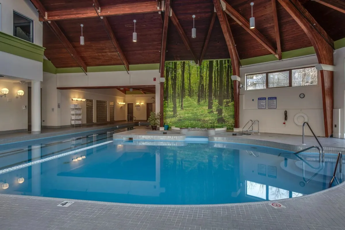 The indoor swimming pool area features a serene setting with a wooden ceiling and a large mural of a forest, merging the feeling of being in nature with indoor comfort. The pool offers a relaxing and rejuvenating atmosphere, perfect for families to unwind after active days.