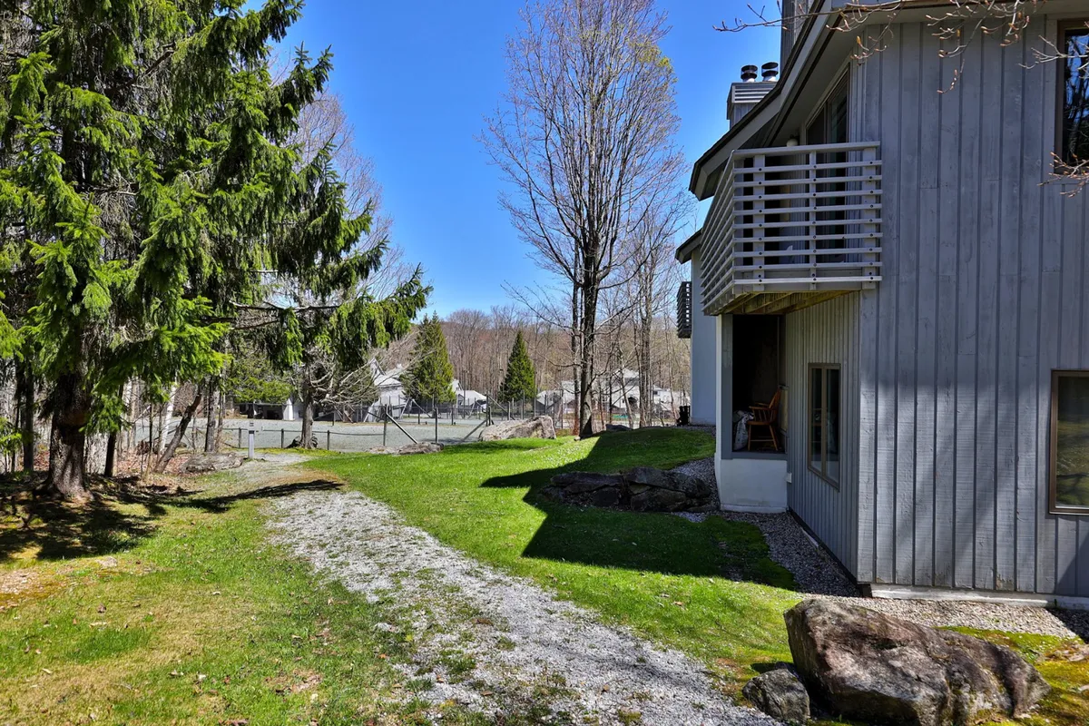 A peaceful exterior scene featuring a pathway winding through lush greenery, leading to a charming balcony. The setting suggests tranquil outdoor strolls and the opportunity to relax outside while surrounded by nature.