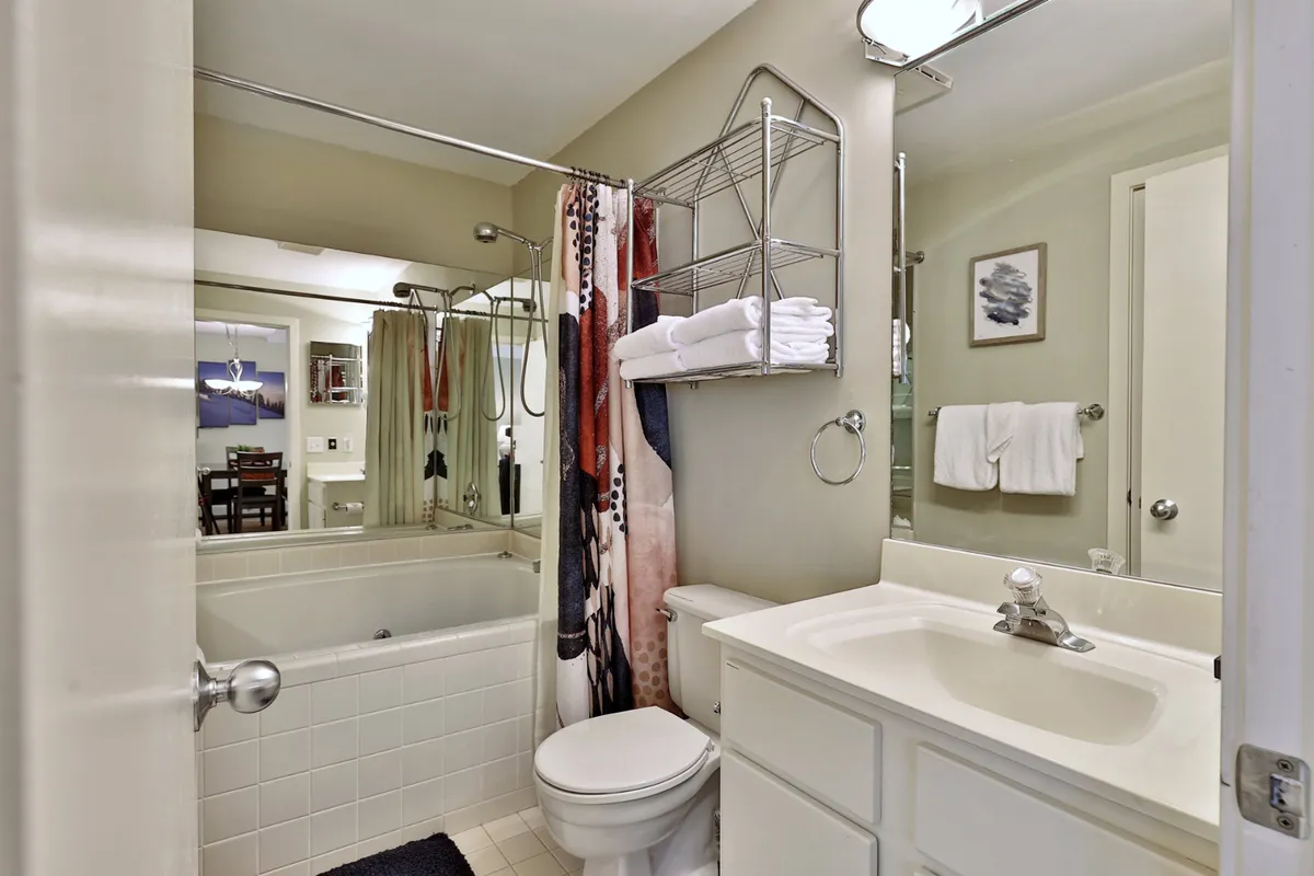 This image centers on a modern bathroom featuring a bathtub, stylish sink, decorative towels, and a large mirror. The ambiance is inviting and functional, with upscale finishes and soft accessories that evoke a spa-like feel. The scene suggests moments of relaxation, whether it's enjoying a soothing bath or preparing for the day in comfort.