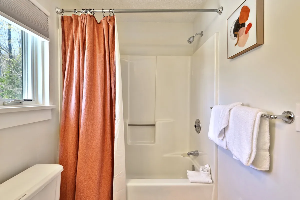 This bathroom image features a calming scene with a bright orange shower curtain, crisp white towels, and tasteful wall art. The space feels serene and welcoming, ideal for a refreshing shower or a relaxing bath after a day outdoors. The decorative elements and soft lighting emphasize comfort and relaxation.